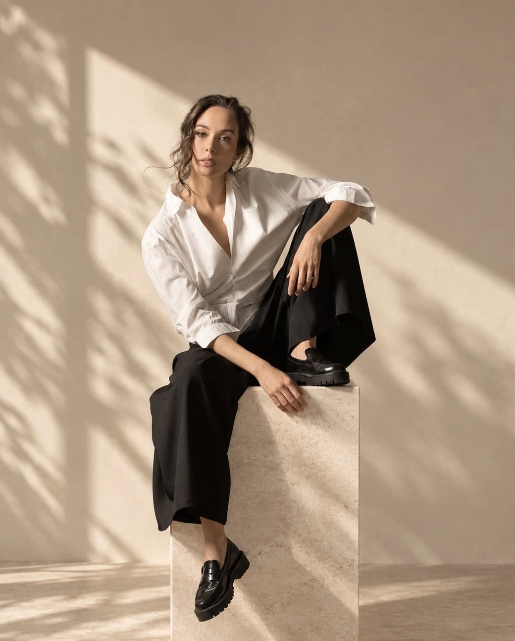 Natalia Lermanda sentada sobre un bloque de travertino, camisa blanca y pantalón negro